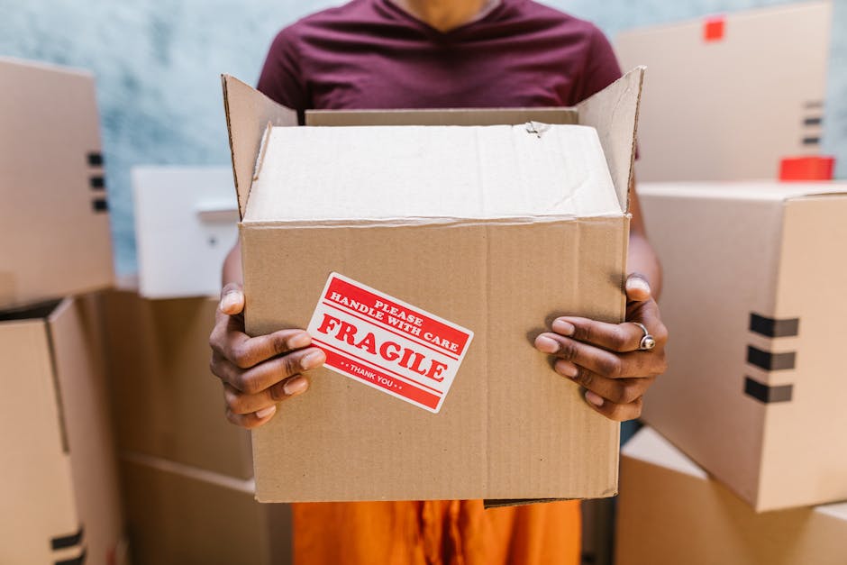 Two movers from Man with Van Newington are carefully transporting a large green velvet sofa with wooden legs outside a building, preparing to load it into a van for a home relocation. The mover on the